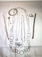 All sterling silver jewelry pieces laid on white backdrop showing interlocking circle necklace, adjustable chain, rope chain, tennis bracelets, pins, and bangle.