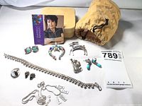 Nine pieces of jewelry including turquoise earrings, Navajo pendant, silver mouse pin, deer brooch, charm bracelet with word pendants, and earrings arranged on white background