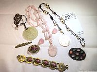 Full overview of the 9 vintage Asian jewelry pieces on a flat surface showing a mix of pendants, beads, and bracelet including carved mother of pearl, rose quartz, brass dragon bracelet, and various carved beads.