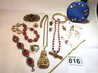 Overview of assorted jewelry pieces laid out on white background including bracelets, necklaces, brooches, rings, earrings, cufflinks