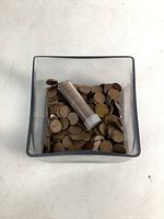 Top view of clear square glass cube with unsorted wheat pennies and a plastic coin roll.
