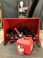 Front view showing steel auger housing with red plastic gas can and fuel stabilizer in front