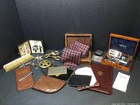 Photo showing a collection of men's accessories including wallets, ties, brass clips, wood boxes, business card holders, and a Nautica box with rings and small items.