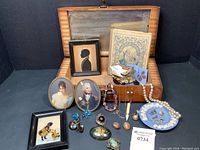 Open wooden jewelry box lined with paper showing mirror and assortment of jewelry, miniatures and booklet