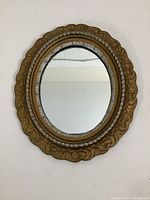 Full view of the oval mirror showing the gold and silver painted cast iron frame with ornate detailing.