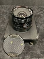 Front angled view of Pentax lens with front lens cap off, showing large glass element and aperture ring markings.