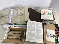 Wide view showing two storage boxes with binders, envelopes, and loose stamps, along with vintage correspondence and information pages related to stamp collecting.