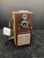 Front view of the brown textured Tom Thumb Radio Camera unit showing camera lens and speaker grille.