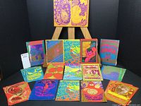 Fifteen postcards arranged front-facing on black background with easel