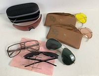 Multiple pairs of vintage glasses including Ray-Ban shooter glasses in cases, aviator style, and pinhole glasses