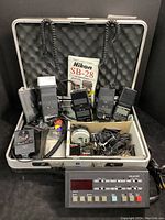 Overall lot contents arranged in open silver carrying case showing multiple flash units, manual, GraLab timer and wired controls