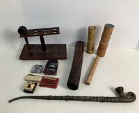 Overview of all lot items laid out on white background: long metal-wood pipe, bamboo chillum, bamboo containers, lighters, wood pipe stand, short wooden pipe.