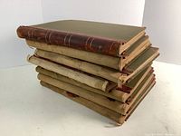 Stack of 7 large hardcover scrapbooks with green covers and brown leather spines, showing signs of wear and age.
