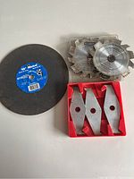 Image showing one 10-inch metal cutting disc, two circular saw blades stacked and a red holder with four dado cutter blades.