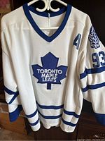 Front view of white CCM Toronto Maple Leafs hockey jersey with blue maple leaf logo, number 93, and Assistant Captain 'A' patch