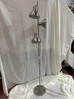 Full view of a vertical floor lamp with a circular base, three dome-shaped adjustable light heads, and a slender metal pole in brushed chrome finish.