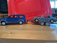 Side view of blue Ford Expedition towing silver Ford Mustang on black dual axle trailer with damaged hitch.