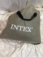 Storage bag for the Intex inflatable bed with black handle and Intex logo in white on beige fabric.