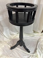Full view of the black wooden plant stand showing the circular top and three-legged base.