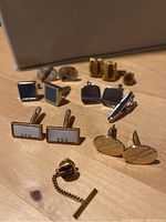 Photo showing assorted cuff links and tie pins with gold, silver tones, mother-of-pearl insets, and various shapes including rectangular, square, and oval.