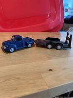 Side view of blue 1948 Ford pickup diecast model and attached black trailer with ramp on wooden surface.