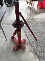 Front view of the red manual tire changer showing the base, vertical post, rotating plate, and lever arm.