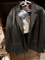 Front view of men's black leather jacket size 3XL by North End with tags on hanger, showing the smooth leather surface, notch lapel, and button closure.