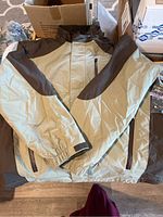Photo of the men's XL ripstop lightweight jacket in espresso and khaki color, laid flat showing front design details including pockets, elastic cuffs, and zipper.