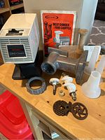 Overall photo showing Rival Grind-O-Matic motor unit, metal grinder body, screw ring, grinder plates, blades, plastic augers and funnels, wooden meat pusher, and product manual.