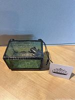 Blue-green stained glass box on wood surface with J. Devlin Glass Art tag visible. Features metal frog on lid and textured glass sides.
