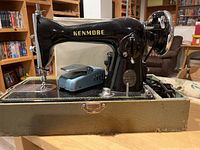 Side view of black Kenmore De Luxe sewing machine with attached foot pedal in green case.