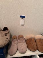 Three pairs of slip-on shoes including beige clogs, beige shearling-lined slippers, and warm brown shearling slippers.