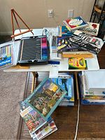 Overview of art supplies and puzzles on small tables including colored pencils, paintbrushes, crayons and puzzles.