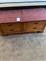 Side view of cedar hope chest showing upholstered mauve lid and two front drawers with metal handles, chest against carpet floor.