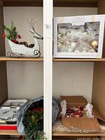 Photo of metal reindeer sleigh decoration, box of handcrafted glass ornaments, greenery wreath, and holly berry serving tray on shelves.
