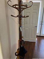 Front view of the wooden coat rack showing the curved top hooks and three umbrellas and cane hanging.