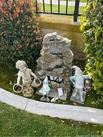 Full view of the garden fountain and figurines arranged on lawn outdoors near a low wall and fence