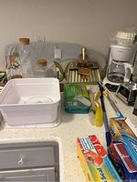 A kitchen counter showing a white mini ironing board, coffee pot, blender, mini fan, mugs on a stand, paper towel dispenser, some kitchen tools and plastic wrap.