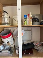 Shelf with stand mixer, buckets, bakeware, spray bottles, and fry pans arranged in garage storage.