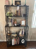 Full view of wrought iron bakers rack with four shelves holding decorative items and books, showing general condition and appearance.