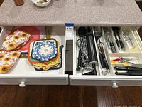 Two drawers, left holds fabric potholders and crocheted doilies, right contains large kitchen utensils organized in white plastic tray.
