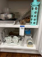 Shelf with kitchenware including stainless steel bowls and pans, clear glass dishes, and milk glass serving set.