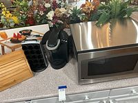 Photo of microwave, Keurig coffee maker with mug holder, wooden breadbox and serving tray together on countertop.