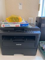 Brother all-in-one printer with Avery sheet protectors on top and yellow bag of miscellaneous office supplies.
