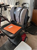 Front three-quarter view of scooter seat, gray backrest cushion and orange instruction manual folder on seat