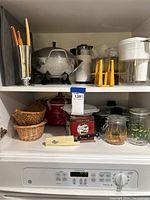 Wide view photo including red crockpot, small scale, serving jars, woven baskets and electric skillet on shelf