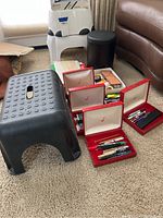 Overview of the plastic step stools, trash can, pen cases and office supplies on carpeted floor against couch