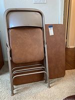 Image showing two brown padded folding chairs stacked against a folded brown rectangular folding table.