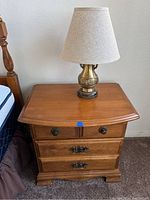 Photo of a maple nightstand with three drawers and a table lamp on top, showing front view and condition.