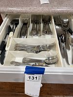 Top view of a kitchen drawer filled with a white plastic utensil tray containing various metal forks, spoons, knives, and serving utensils.